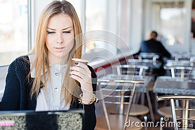 Beautiful young blond business woman sitting in a coffee shop drinking coffee and working on laptop computer pc Stock Photo