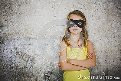 Blond girl with black superhero mask and yellow shirt is posing in front of concrete background Stock Photo