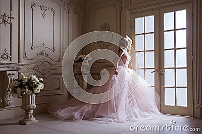 Beautiful young blond woman in luxurious long pink dress posing in vintage room interior Stock Photo