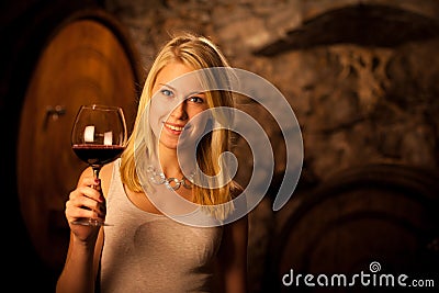 Beautiful young blond woman tasting red wine in a wine cellar Stock Photo