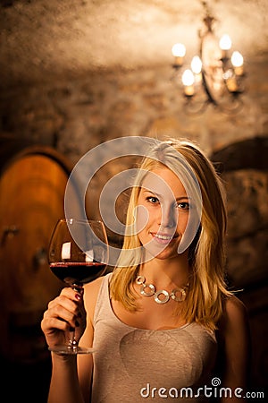 Beautiful young blond woman tasting red wine in a wine cellar Stock Photo
