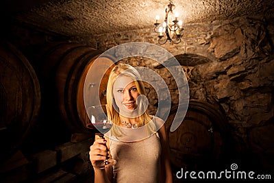 Beautiful young blond woman tasting red wine in a wine cellar Stock Photo