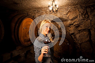 Beautiful young blond woman tasting red wine in a wine cellar Stock Photo