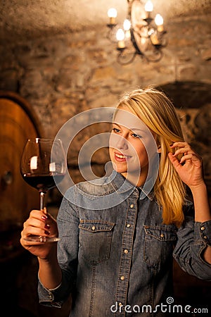 Beautiful young blond woman tasting red wine in a wine cellar Stock Photo