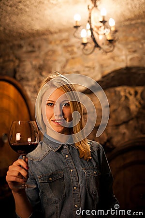 Beautiful young blond woman tasting red wine in a wine cellar Stock Photo