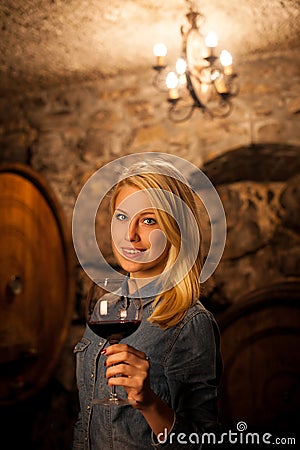 Beautiful young blond woman tasting red wine in a wine cellar Stock Photo