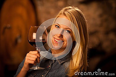 Beautiful young blond woman tasting red wine in a wine cellar Stock Photo