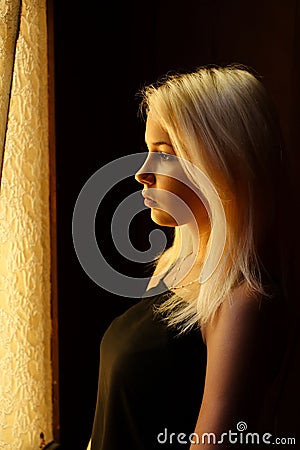 Beautiful young blonde girl. Dramatic portrait of a woman in the dark. Dreamy female look in twilight. Female silhouette. Stock Photo