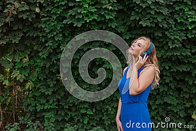 Beautiful young blonde girl in a dress listening to music in blue headphones. Real life, enjoy the moments. Copy space Stock Photo