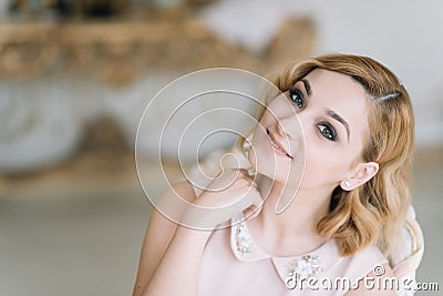 Beautiful young blonde girl in a pink dress smiles in a bright room in the morning Stock Photo