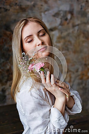 A beautiful young blonde woman holds carnation and gypsophila flowers in her hands near her face Stock Photo