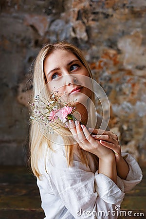 A beautiful young blonde woman holds carnation and gypsophila flowers in her hands near her face Stock Photo