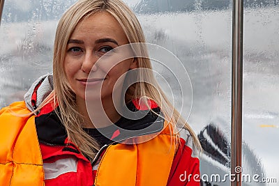 Beautiful young blonde woman in an orange life jacket sits in a motor boat during an excursion and sailing on Lake Teletskoye in Stock Photo