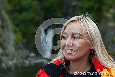 Beautiful young blonde woman in an orange life jacket sits in a motor boat during an excursion and sailing on Lake Teletskoye in Stock Photo
