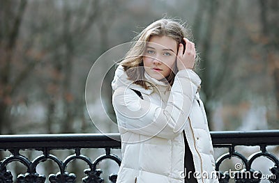 Beautiful young blonde woman standing on the spring city park in warm clothes. Cold season lifestyle freshness concept Stock Photo