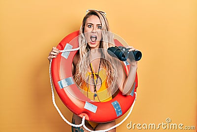 Beautiful young blonde woman wearing bikini and holding lifeguard float and binoculars celebrating crazy and amazed for success Stock Photo