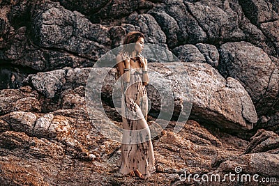 Beautiful young boho style woman on stones background at sunset Stock Photo