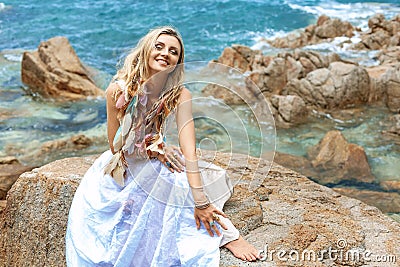 Beautiful young boho style woman in white dress on stone beach Stock Photo