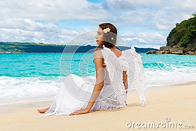 Beautiful young bride with angel wings on the sea coast. Tropical sea in the background. Stock Photo