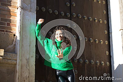 beautiful young brunette woman with curly hair and green woollen coat is standing at the entrance of a building in seville, spain Stock Photo