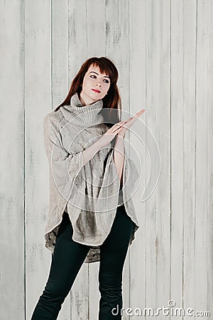 A beautiful young brunette woman in a gray pullover, looking sideway thoughtfully, with light background wall. Emotional female Stock Photo