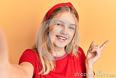 Beautiful young caucasian girl taking a selfie photo smiling happy pointing with hand and finger to the side Stock Photo