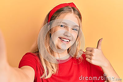 Beautiful young caucasian girl taking a selfie photo smiling happy and positive, thumb up doing excellent and approval sign Stock Photo