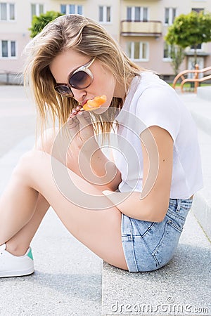 Beautiful young cheerful happy girl eating ice cream , smiling in shorts and a white T-shirt on the area on a bright sunny day Stock Photo