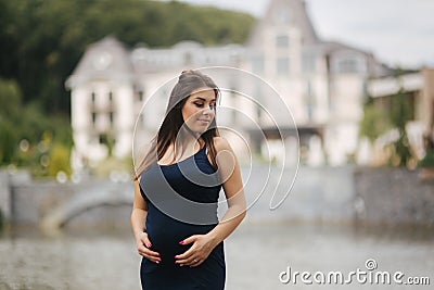 Beautiful young cheerful pregnant woman standing in background of fountain. six months of pregnancy. She pu her hands on Stock Photo