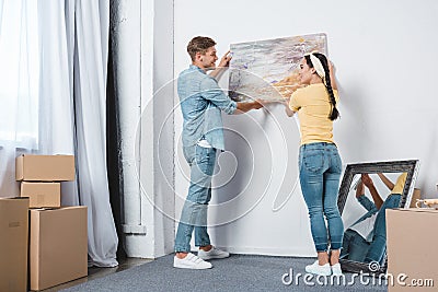 beautiful young couple hanging picture on wall together while moving into Stock Photo