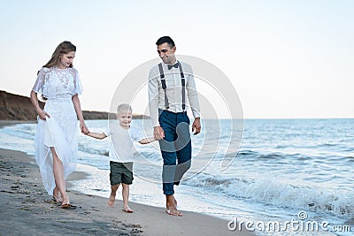 Beautiful Young couple with little boy walks on the beach. Parents keep son`s hands Stock Photo