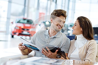 Beautiful young couple looking a new car at the dealership showroom. Stock Photo