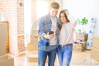 Beautiful young couple moving to a new house using smartphone stressed with hand on head, shocked with shame and surprise face, Stock Photo