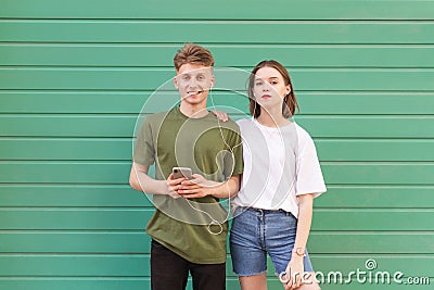 Beautiful young couple standing on the background of a green wall in the headphones, looking at the camera. Nice guy and a girl Stock Photo
