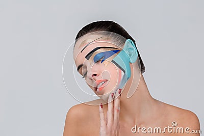 A young girl with a geometric make-up closed eyes and tucked head. On a gray background. Stock Photo