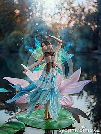 Beautiful young fantasy woman in the image of a river fairy dances on a water lily flower. A long silk dress flies in Stock Photo