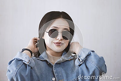 Beautiful young fashionista girl in trendy jeans jacket and sunglasses. Portrait of attractive and cute female smiling to the Stock Photo