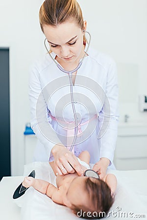 Beautiful young female blonde pediatrician doctor examines baby girl with stethoscope checking heart beat. baby is lying on the Stock Photo