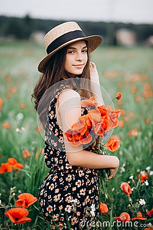 Beautiful young free girl in a hat in a summer field of red poppies with a bouquet. Soft selective focus Stock Photo