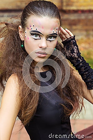 Beautiful young girl on the background of the leaves in autumn day on the street with fantasy makeup in a black dress Stock Photo