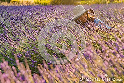 The beautiful young girl in a blue dress and cap sits in a lavender flowers, long curly hair, smile, pleasure, a house Stock Photo