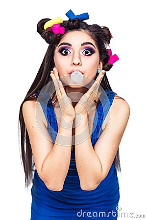 Beautiful young girl in a blue dress with curlers inflates a bubble of chewing gum. Stock Photo