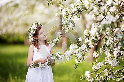 Beautiful young girl in blue dress in the garden with blosoming apple trees. Cute girl holding apple-tree branch Stock Photo