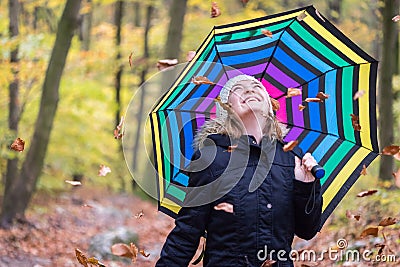 Beautiful young girl with colorful umbrella is enjoying the dropping leaves in the autumnal forest Stock Photo
