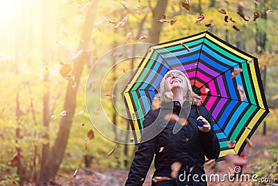 Beautiful young girl with colorful umbrella is enjoying the dropping leaves in the autumnal forest Stock Photo