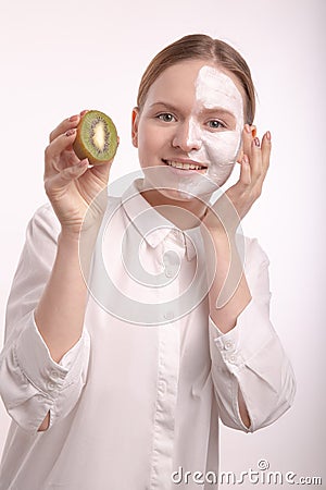 Beautiful young girl with a cream mask on her face holding a kiwi. Stock Photo