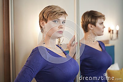 The beautiful young girl with curvy figure and short hair in fashion dress near the mirror Stock Photo
