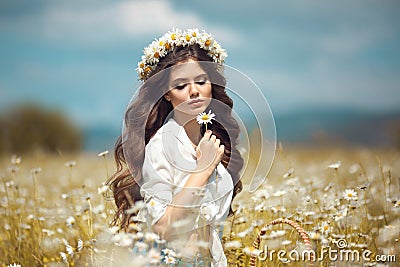 Beautiful young girl with flower enjoying in chamomile field. Carefree happy brunette woman with chaplet on healthy wavy hair Stock Photo