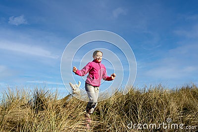 Portrait of a beautiful young girl and her puppy running on the sand dunes Stock Photo