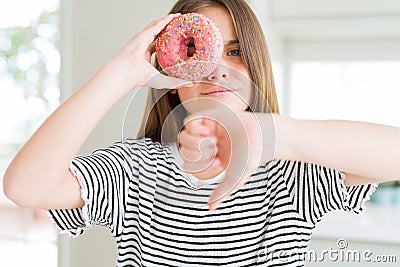 Beautiful young girl kid eating sweet pink donut with angry face, negative sign showing dislike with thumbs down, rejection Stock Photo